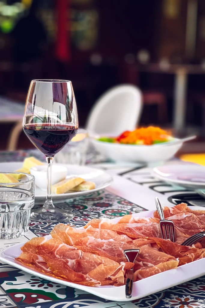 Piatto di prosciutto di San Daniele accompagnato da un calice di vino rosso.