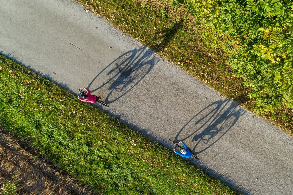 Due ciclisti percorrono un percorso asfaltato proiettando le loro ombre